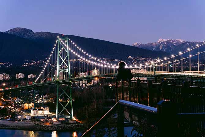 Lion's Gate Bridge lit up at night, with the North Shore Mountains in the background
